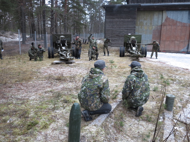 Nuoret tykkimiehet Teemu Lahdensuo ja Aaro Siniketo. Kranaatti vasemmalla on puinen "mock-up" ja. harmaa lieriö oikealla on sen matkaan lennättävä panos, tosin nyt vielä ilmatiiviissä säilytyskotelossaan.